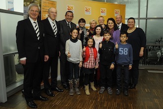 Eine Gruppe von Erwachsenen und Kindern steht lächelnd vor einer Wand mit dem Logo der DFL Stiftung.