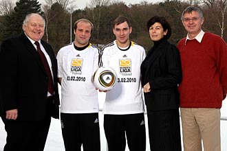 Vier Personen stehen im Schnee und halten einen Fußball. Zwei Fußballspieler tragen weiße Trikots mit dem Aufdruck "LIGA 11.02.2010" und "LIGA 11.02.2010". Links und rechts stehen zwei weitere Personen, vermutlich Vertreter der DFL Stiftung und der Lebenshilfe.
