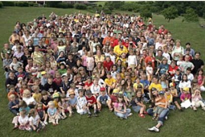 Eine große Gruppe von Kindern und Jugendlichen posiert für ein Gruppenfoto auf einer grünen Wiese. Viele Gesichter sind zu sehen, die Teilnehmer eines Seminars oder einer Veranstaltung der DFL Stiftung.