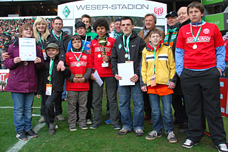 Eine Gruppe von Kindern und Betreuern steht auf dem Rasen des Weserstadions Bremen. Einige Kinder halten Urkunden oder Medaillen in den Händen. Im Hintergrund sind Zuschauer auf den Tribünen zu erkennen.