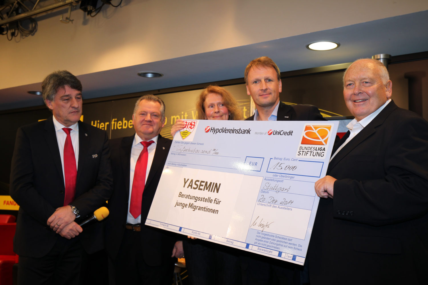 Fünf Männer halten einen übergroßen Scheck mit dem Aufdruck "15.000 EUR" und dem Logo der Bundesliga-Stiftung. Der Scheck ist an "Yasemin - Beratungsstelle für junge Migrantinnen" adressiert. Im Hintergrund sind Logos von HypoVereinsbank und UniCredit zu sehen.
