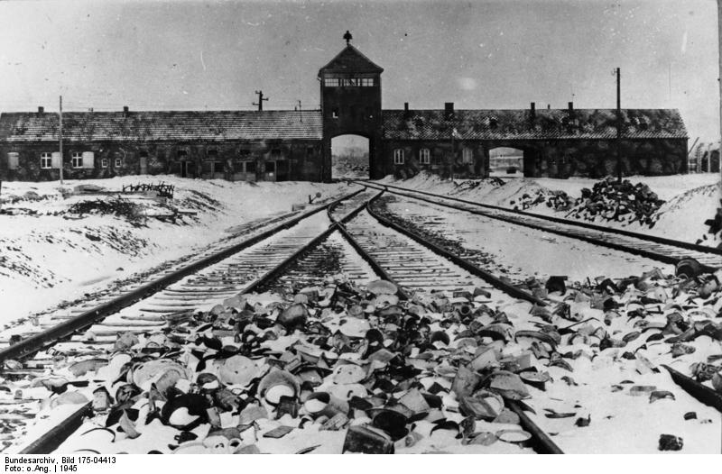 Die Gleise der Rampe in Auschwitz-Birkenau nach der Befreiung im Januar 1945 sind mit unzähligen Kleidungsstücken, Schuhen und Gepäckstücken bedeckt, die von den deportierten und ermordeten Menschen zurückgelassen wurden. Im Hintergrund ist das Tor des Konzentrationslagers zu sehen.