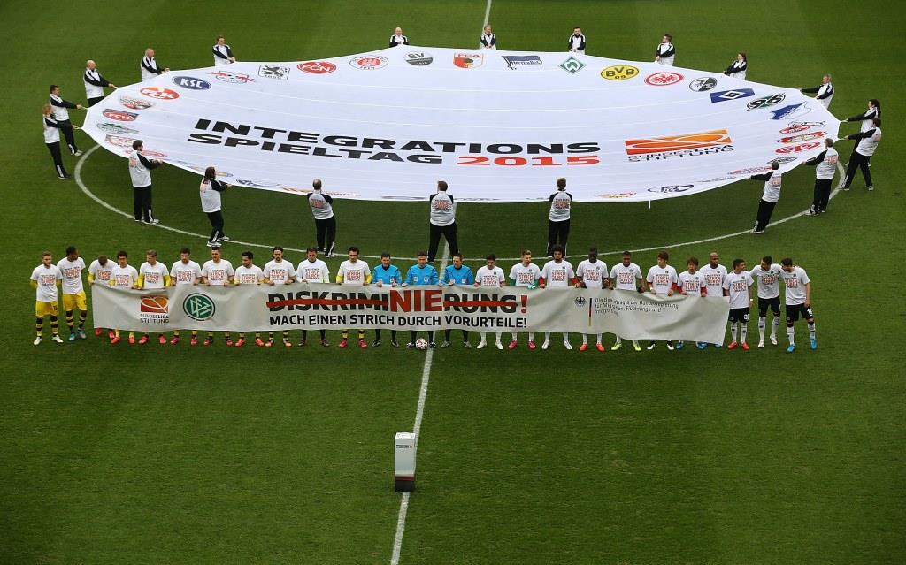 Spieler von Hannover 96 und Borussia Dortmund halten vor Spielbeginn ein großes Banner mit der Aufschrift "DISKRIMINIERUNG! MACH EINEN STRICH DURCH VORURTEILE!" auf dem Rasen.
