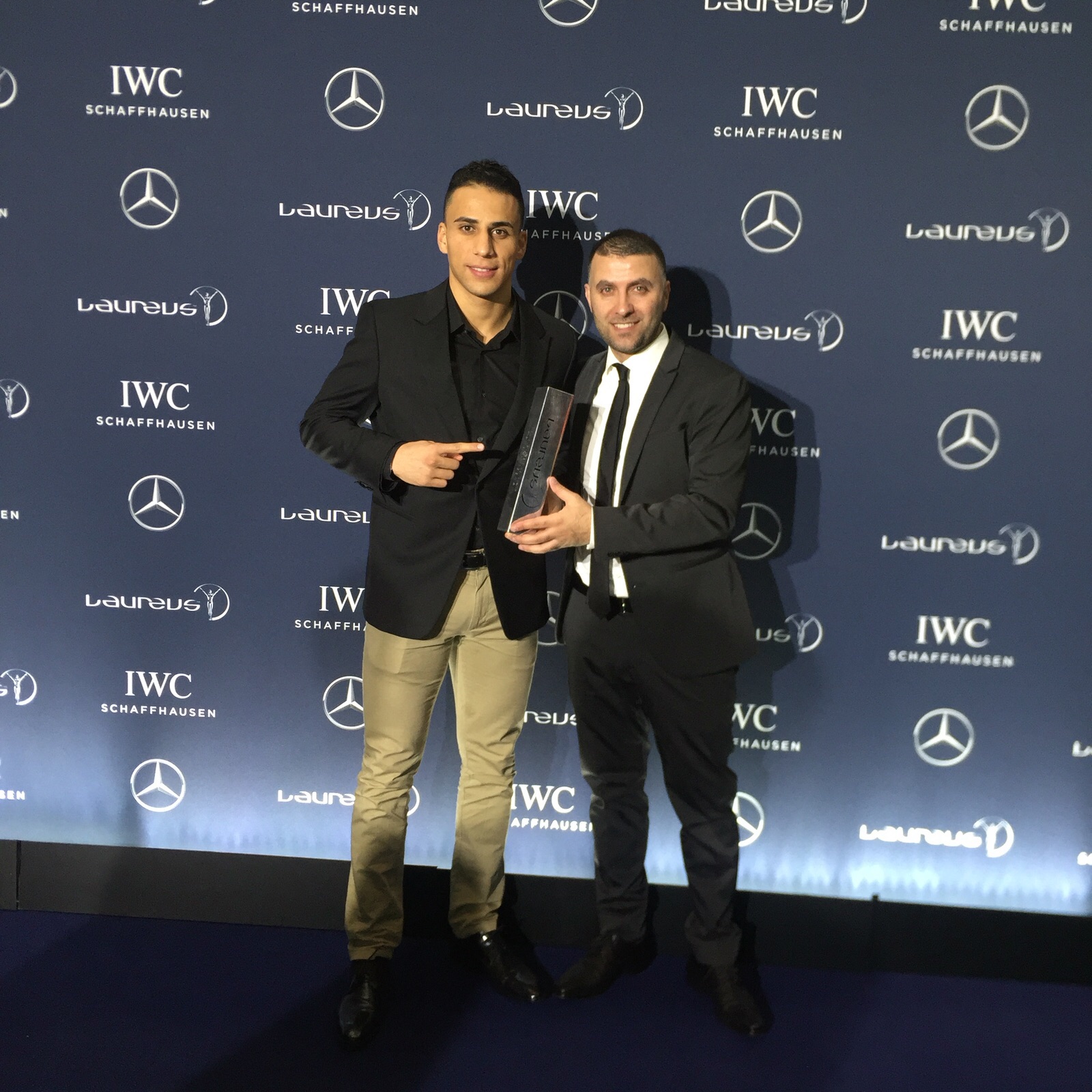 Zwei Männer, vermutlich Fußballspieler, halten eine Auszeichnung in den Händen und posieren auf einem roten Teppich vor einer Wand mit den Logos von IWC Schaffhausen und Laureus.