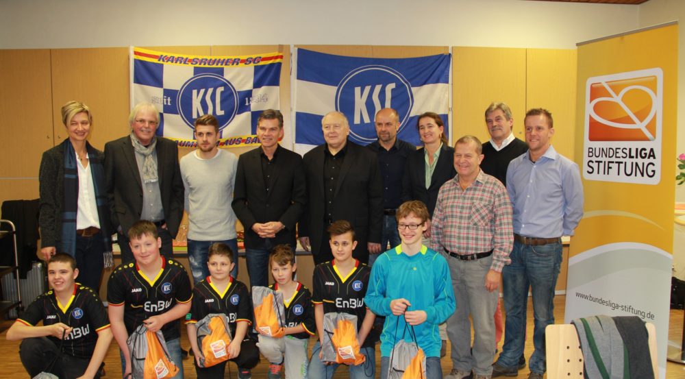 Eine Gruppe Jugendfußballspieler im Trainingsoutfit des Karlsruher SC steht mit Vertretern der Bundesliga-Stiftung für ein Gruppenfoto. Im Hintergrund ist ein Banner mit dem Logo der Bundesliga-Stiftung zu sehen.