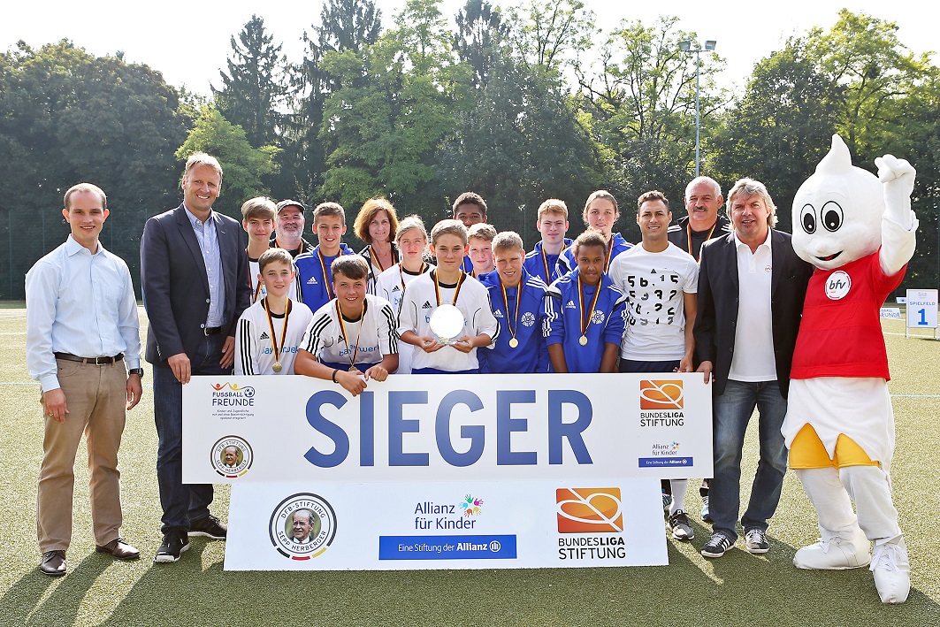 Mannschaft des Teams "Marktheidenfeld" mit Silbermedaillen und Siegerbanner bei einem inklusiven Fußballturnier der DFL Stiftung. Neben der Mannschaft stehen Vertreter der DFL Stiftung und Allianz. Auf dem Banner steht "SIEGER". Das Maskottchen der DFL Stiftung steht am rechten Bildrand.