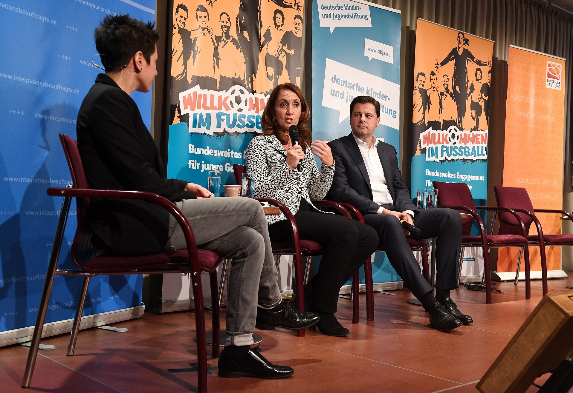 Dunja Hayali, Aydan Özoguz (Bundesbeauftragte für Migration, Flüchtlinge und Integration) und Christian Seifert (Vorsitzender der Geschäftsführung DFL) sitzen auf einer Bühne und diskutieren im Rahmen der Veranstaltung "Willkommen im Fussball – Mit dem Fussball in die Mitte der Gesellschaft".