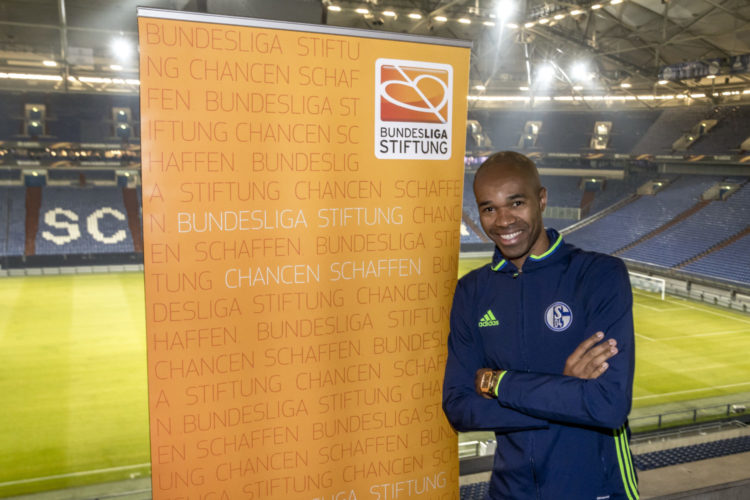 Naldo, ehemaliger Fußballspieler, posiert als Integrationspate vor einer großen Bannerwand mit der Aufschrift "Bundesliga Stiftung Chancen schaffen". Im Hintergrund ist ein Fußballstadion zu sehen.