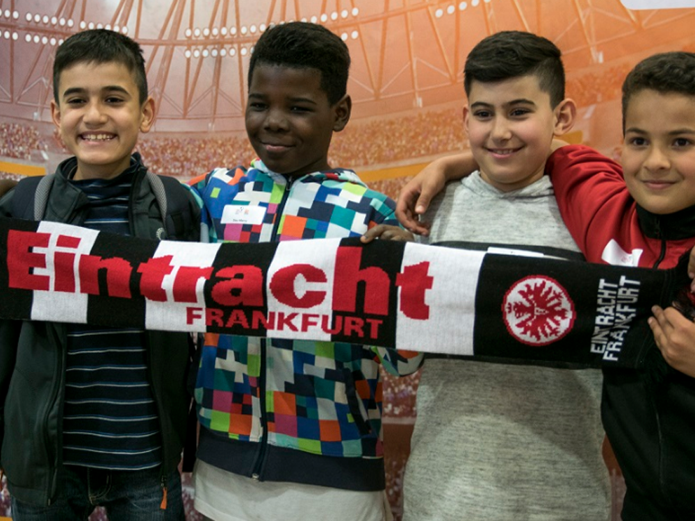 Vier lächelnde Jungen umarmen sich und halten gemeinsam ein Banner mit dem Aufdruck "Eintracht Frankfurt".