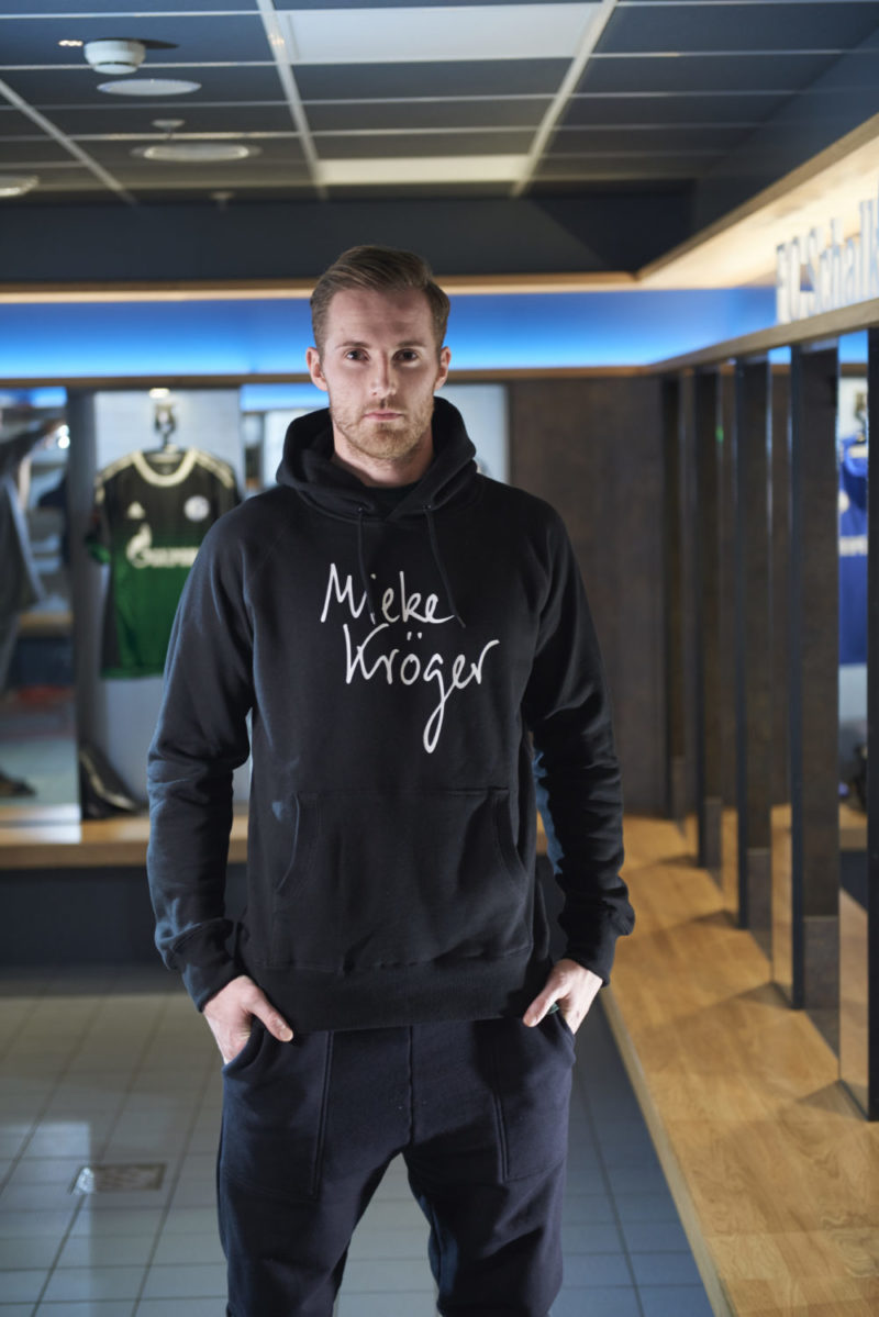 Ralf Fährmann, Torwart, in den Umkleideräumen der Veltins Arena auf Schalke, trägt einen schwarzen Hoodie und eine schwarze Trainingshose.