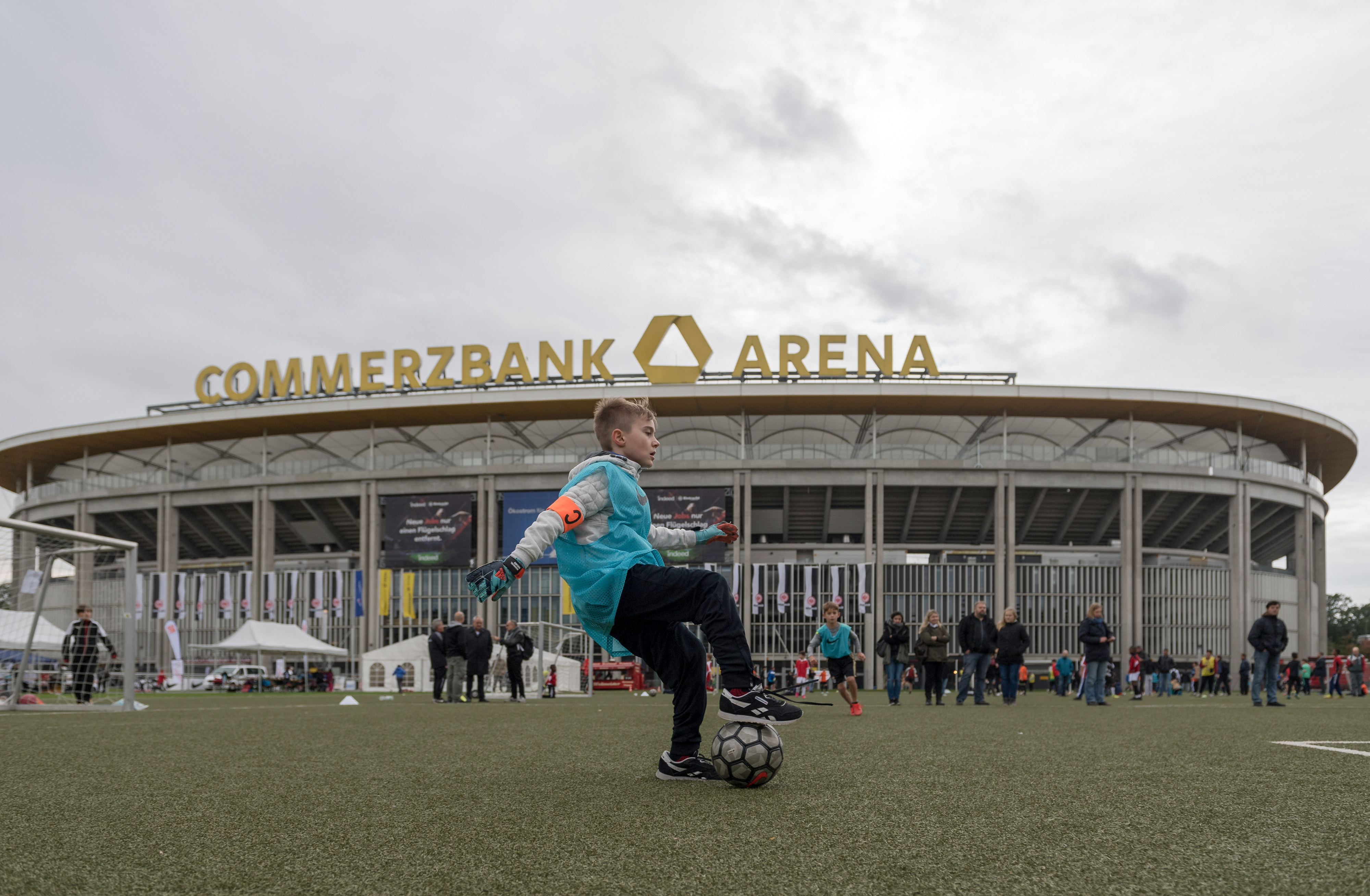 Ein Junge jongliert auf einem Fußballplatz vor der Commerzbank-Arena in Frankfurt. Im Hintergrund sind weitere Personen und Zelte zu sehen.