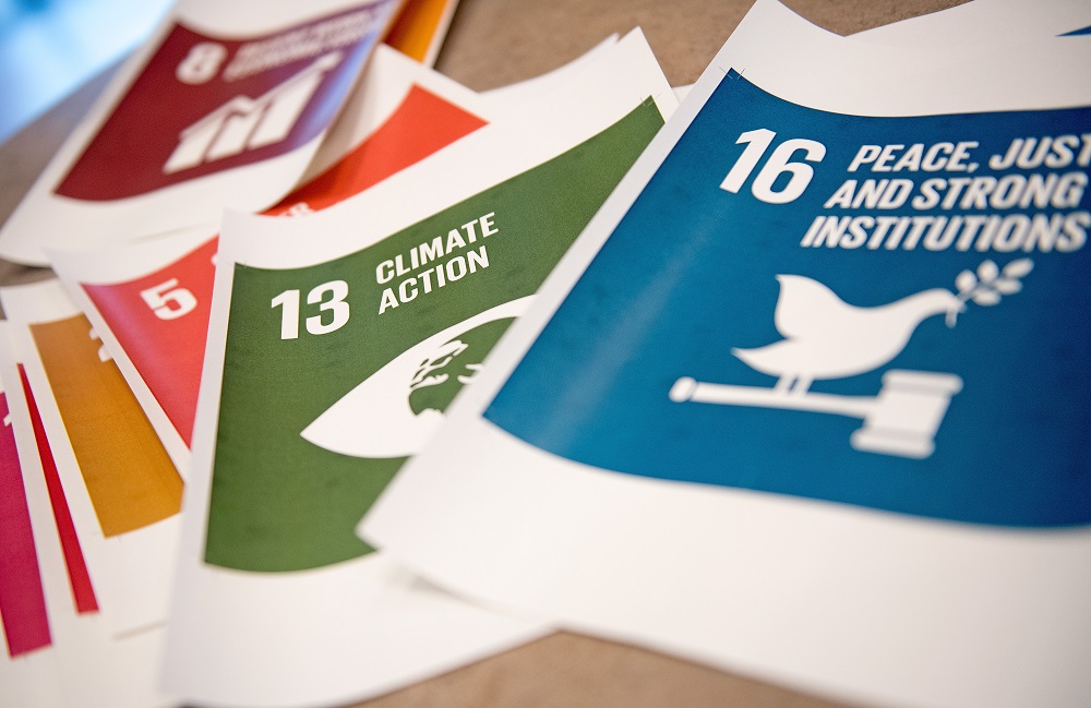 Alt-Text: Mehrere Karten mit den Zielen für nachhaltige Entwicklung der Vereinten Nationen liegen übereinander, darunter die Ziele 13 (Klimaschutz) und 16 (Frieden, Gerechtigkeit und starke Institutionen).