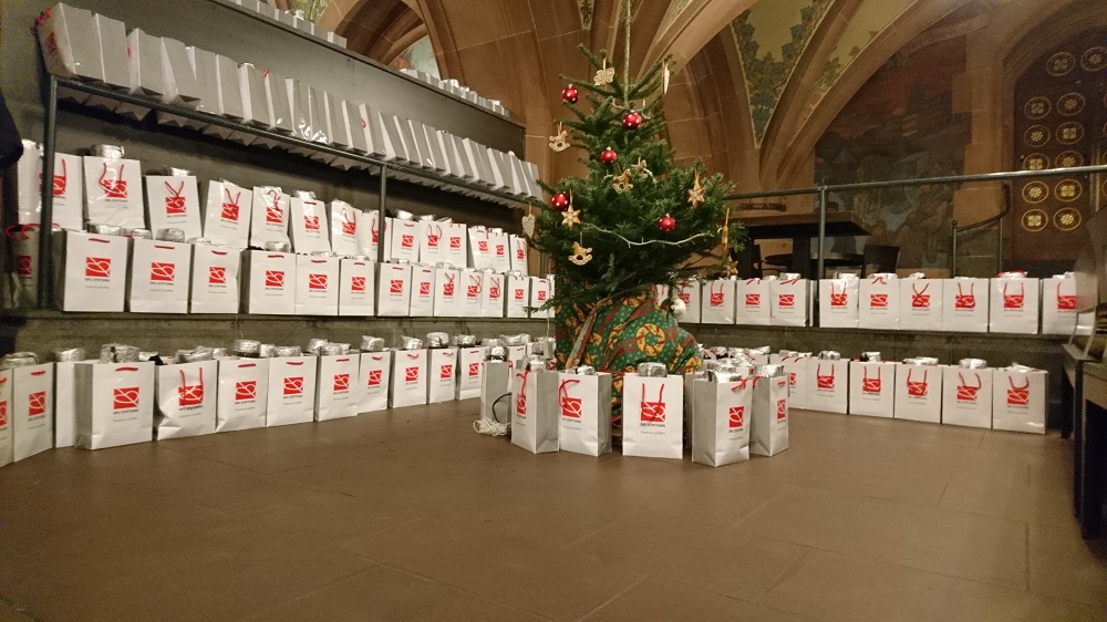 Verpackte Essen stehen in einer großen Anzahl auf dem Boden eines Raumes mit Gewölbedecken, vor einem geschmückten Weihnachtsbaum.