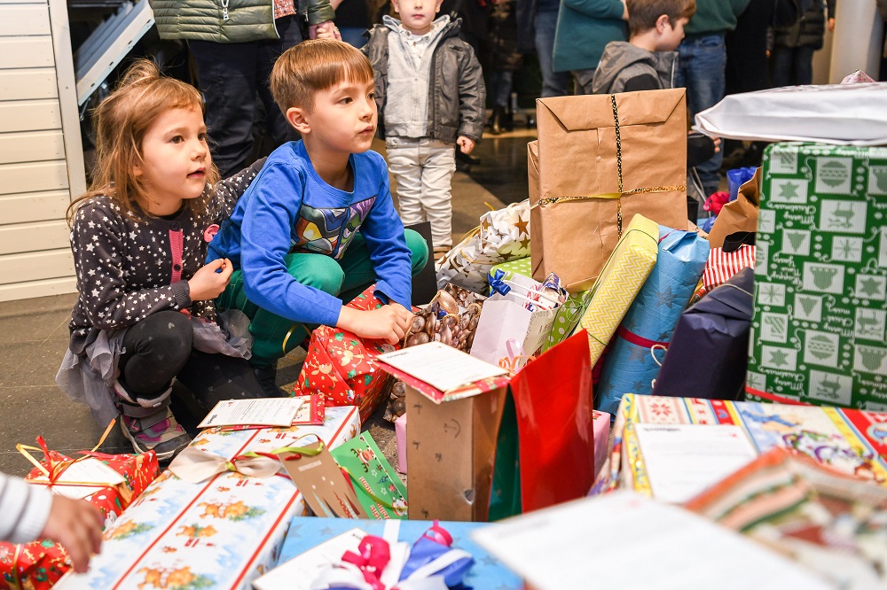Zwei Kinder betrachten gespannt einen großen Haufen bunt verpackter Geschenke, die von der DFL Stiftung und Bullyland für den Verein Kinderlachen e.V. gespendet wurden.