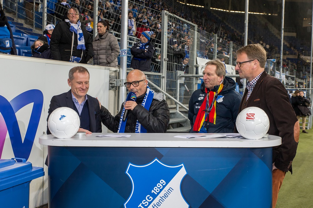 Gesprächsrunde mit Dr. Peter Görlich (TSG-Geschäftsführer), Michael Mildenberger (Vorsitzender Integrativer TSG-Fanclub) und Stefan Kiefer (Vorstandsvorsitzender DFL Stiftung) an einem Tisch mit TSG-Logo und Fußbällen im Hintergrund.