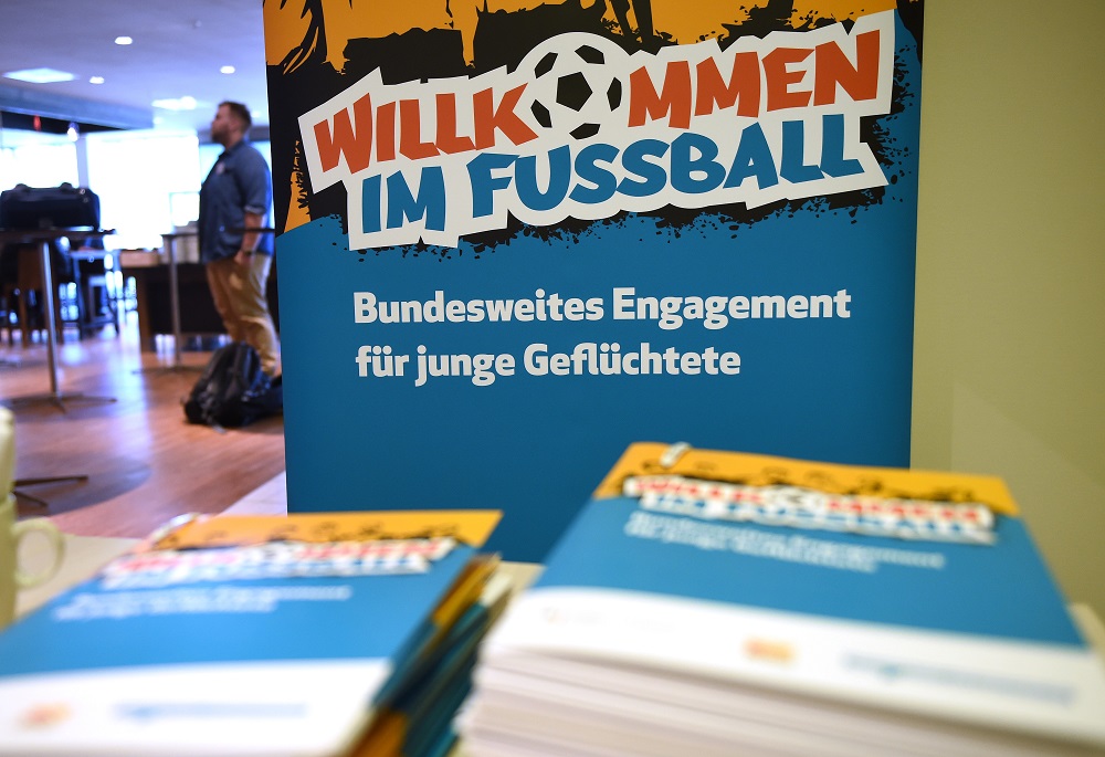 "Willkommen im Fußball" steht auf einem Banner im Hintergrund, während im Vordergrund Exemplare der Dokumentation zur Fachveranstaltung 2018 liegen.