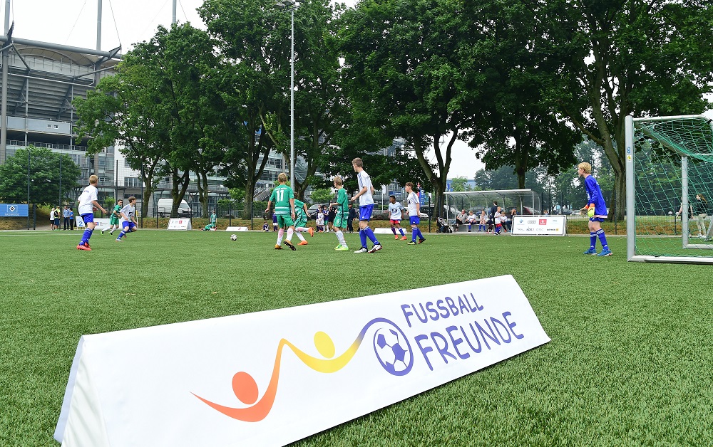 Fußballspiel im Rahmen des Inklusionsturniers "Der Hamburger Weg" mit Kindern und Jugendlichen auf einem grünen Kunstrasenplatz. Im Vordergrund ein Werbebanner mit dem Logo "FußballFreunde".
