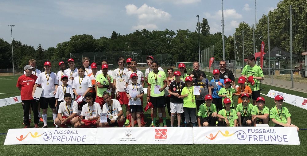 Gruppenfoto der teilnehmenden Mannschaften des FußballFreunde-Cups Südwest in Mainz, mit Medaillen und Urkunden, vor einer Werbeplane mit dem Logo der DFL Stiftung und "FußballFreunde".