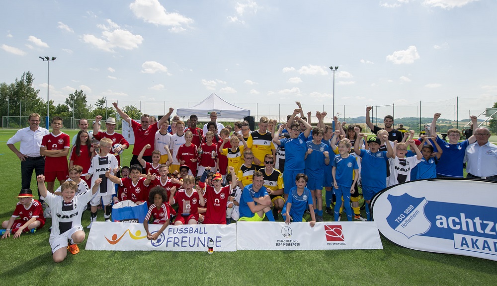 Eine Gruppe von Kindern und Jugendlichen mit und ohne Behinderung steht auf einem Fußballfeld vor einer Werbeplane und jubelt in die Kamera. Im Hintergrund ist ein Fußballtor zu sehen. Die DFL Stiftung unterstützt das Turnier "FußballFreunde-Cup" gemeinsam mit der DFB-Stiftung Sepp Herberger.