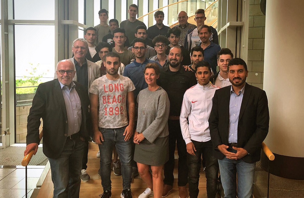 Gruppe von jungen Menschen und ein älterer Herr stehen auf einer Treppe in einem modernen Gebäude, vermutlich im Düsseldorfer Landtag. Sie lächeln in die Kamera. Der ältere Herr trägt einen Anzug, die jungen Menschen sind leger gekleidet.