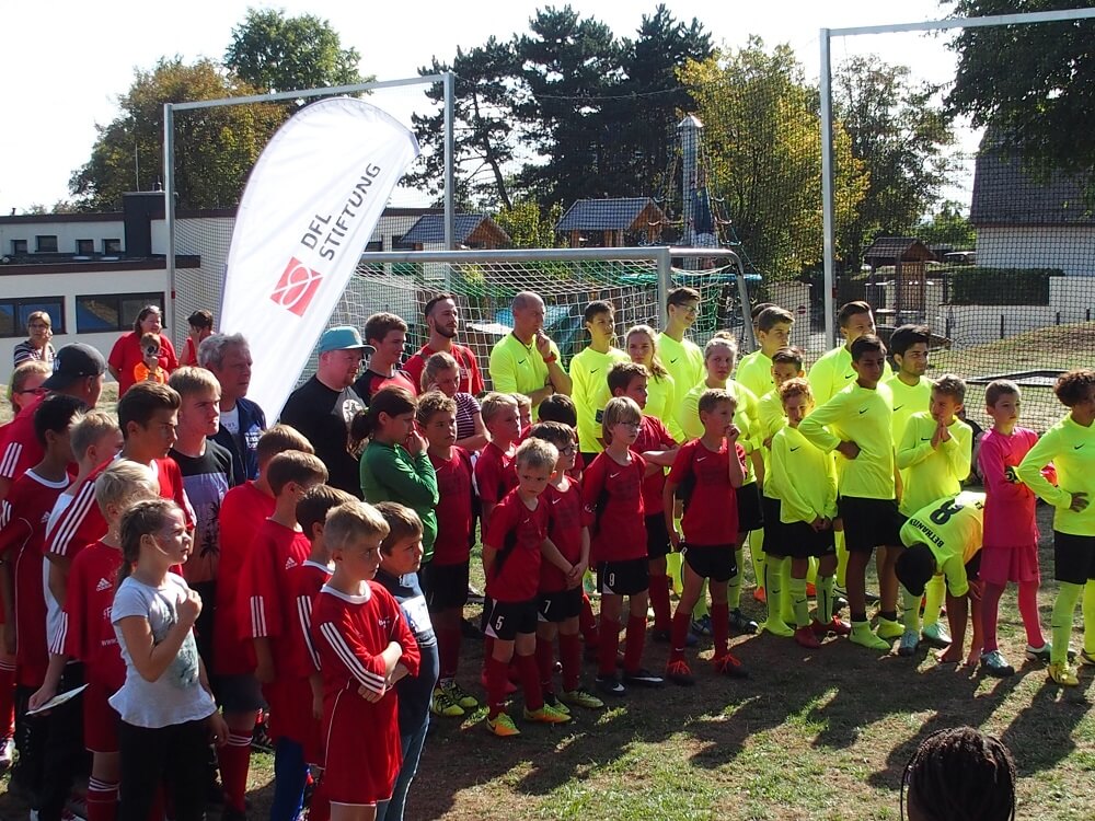 Fußballmannschaften mit Kindern stehen auf einem Fußballfeld vor einer Werbeplane der DFL Stiftung.