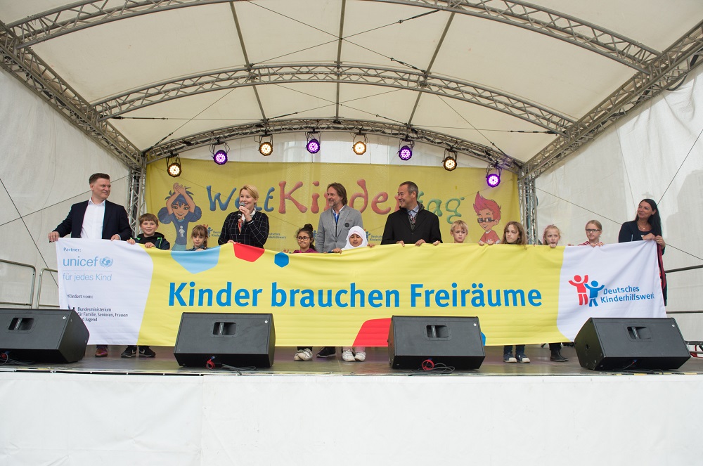 Gruppenfoto auf der Bühne des Bundeszentralen Weltkindertagsfestes mit Dr. Franziska Giffey, der Bundesministerin für Familie, Senioren, Frauen und Jugend, und weiteren Personen. Im Hintergrund ein Banner mit der Aufschrift "Kinder brauchen Freiräume" und Logos von UNICEF und dem Deutschen Kinderhilfswerk.