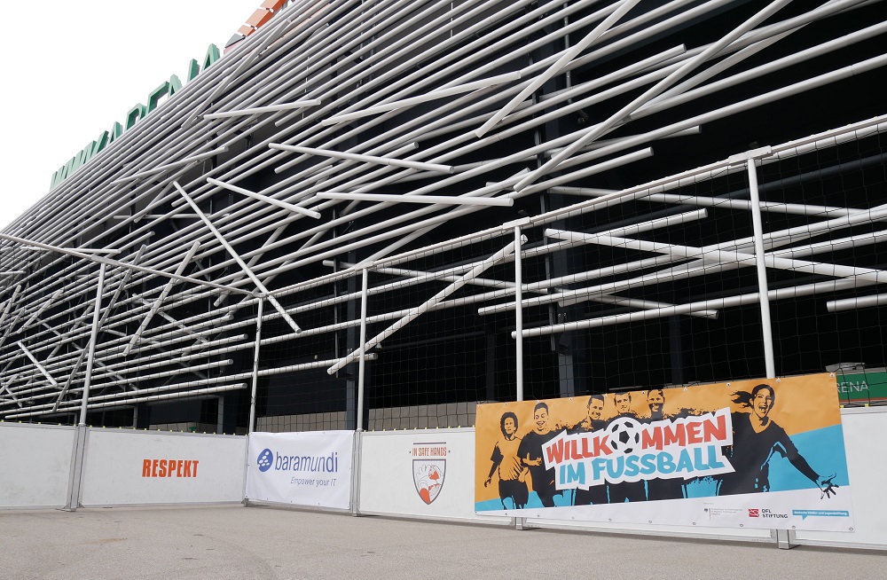 Straßenfußballturnier "Willkommen im Fußball" vor der WWK Arena in Augsburg: Banner mit lächelnden Menschen und dem Schriftzug "Willkommen im Fußball" vor der Fassade des Stadions.