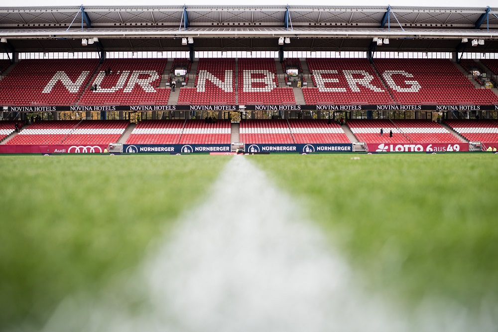 Das leere Fußballstadion des 1. FC Nürnberg vor einem Bundesliga-Spiel, Blick auf die Zuschauertribünen und den grünen Rasen.