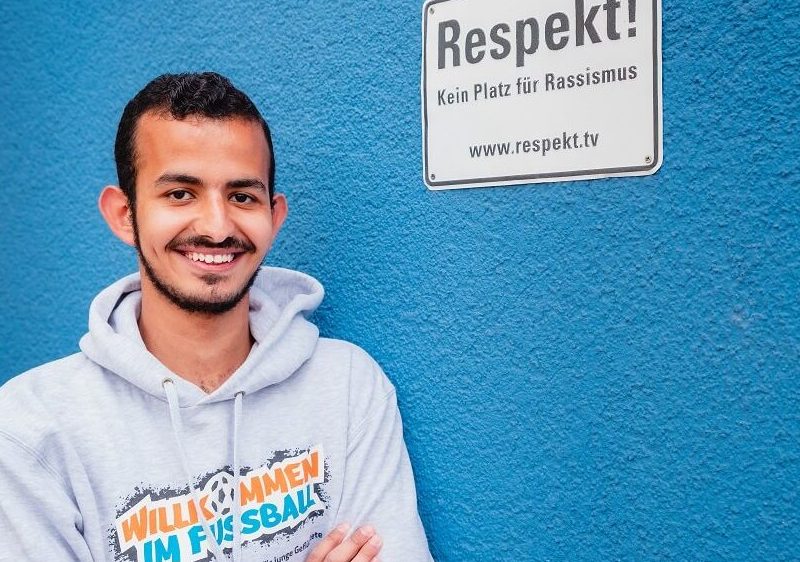 Der Junge lehnt sich an die blaue Wand mit dem Schild, der dazu auffordert, keinen Platz für Rassismus zu lassen.