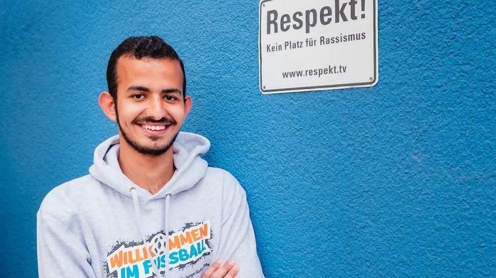 Der Junge lehnt sich an die blaue Wand mit dem Schild, der dazu auffordert, keinen Platz für Rassismus zu lassen.