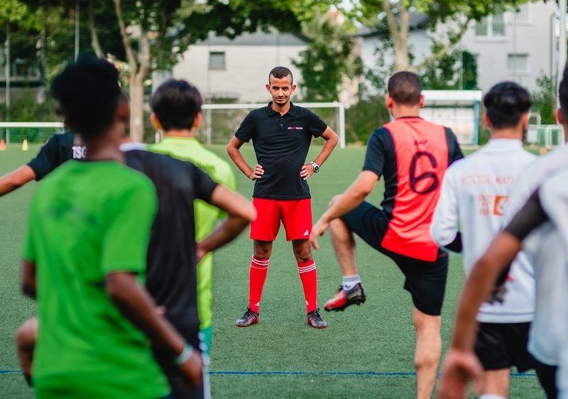 Der Trainer steht vor dem Team auf einem Fußballfeld.