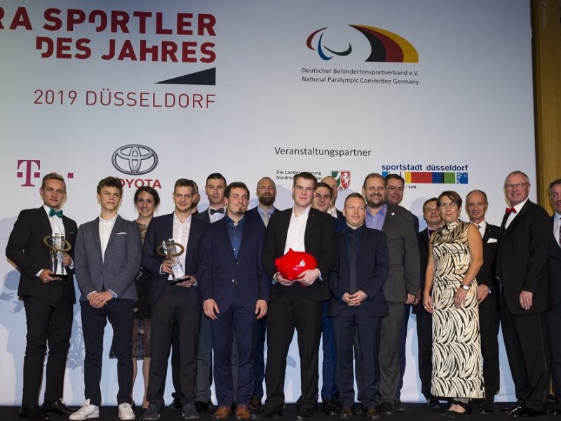 Para-Sportler des Jahres 2019: Gruppe von Athleten und Funktionären posieren auf der Bühne mit den goldenen Trophäen in Düsseldorf. Im Hintergrund Banner mit dem Logo des Deutschen Behindertensportverbands und Veranstalterlogos.