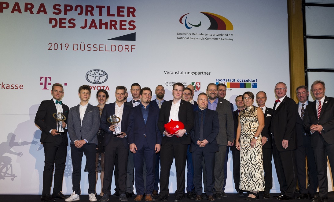Para-Sportler des Jahres 2019: Gruppe von Athleten und Funktionären posieren auf der Bühne mit den goldenen Trophäen in Düsseldorf. Im Hintergrund Banner mit dem Logo des Deutschen Behindertensportverbands und Veranstalterlogos.