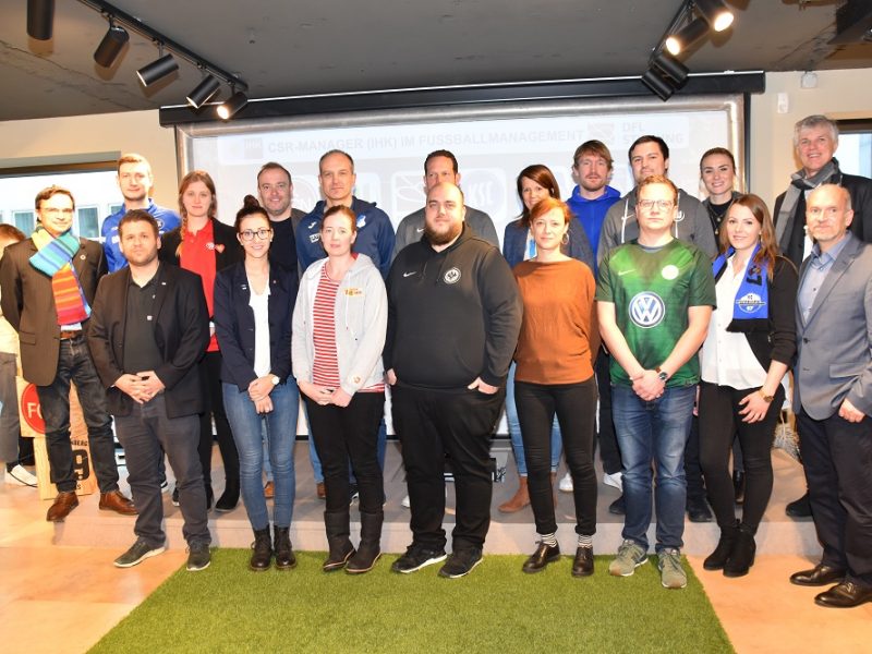 Eine Gruppe von ca. 20 Personen steht lächelnd für ein Gruppenfoto zusammen. Die Teilnehmer der Fortbildung tragen verschiedene Kleidungsstile, von formeller bis leger. Im Hintergrund ist ein Fenster mit Tageslicht zu sehen.