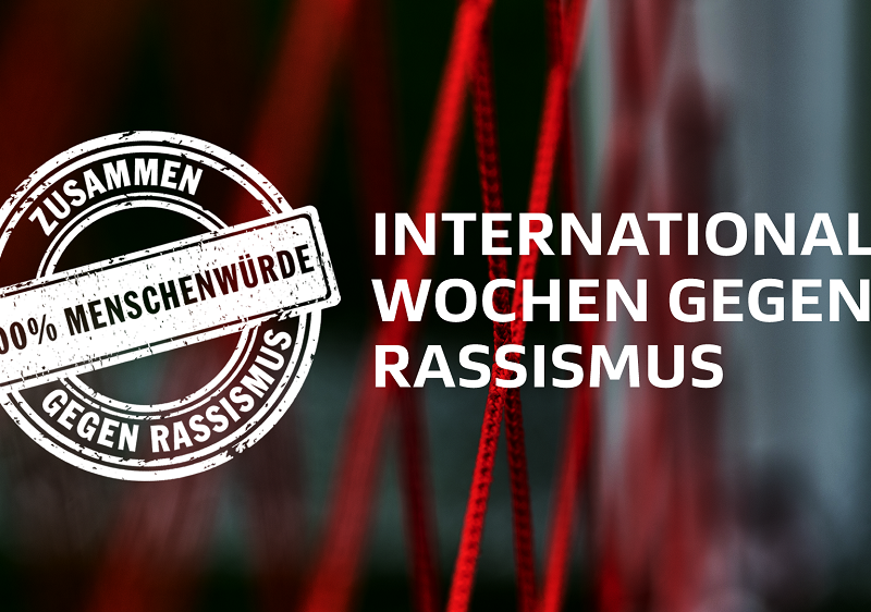 "Logo '100% Menschenwürde – Gegen Rassismus' vor rotem, verschwommenem Hintergrund mit dem Text 'Internationale Wochen gegen Rassismus'."