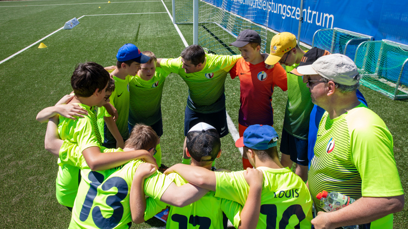 Eine Fußballmannschaft steht auf dem Rasen im Kreis zusammen. Die Spieler haben die Arme über die Schultern der Mitspieler gelegt.