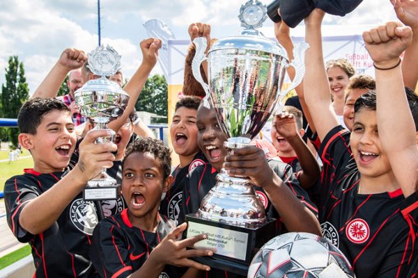 A group of boys and girls in Eintracht Frankfurt jerseys cheer and rejoice over winning the