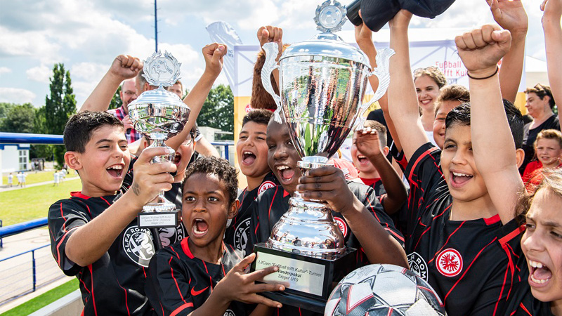 A group of boys and girls in Eintracht Frankfurt jerseys cheer and rejoice over winning the 
