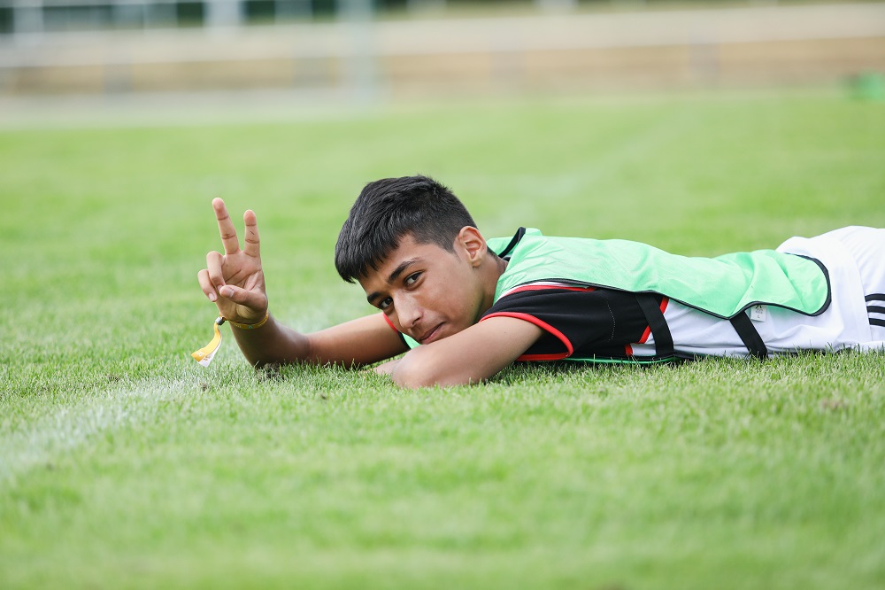 Ein Junge liegt auf dem Rasen und zeigt das Friedenszeichen mit seinen Fingern