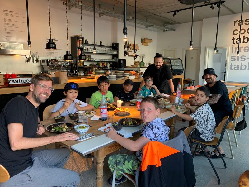 Drei Männer und und sechs Jungen sitzen am Esstisch und essen