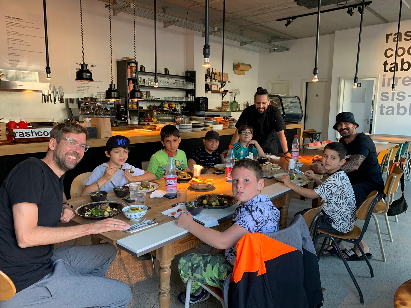 Drei Männer und und sechs Jungen sitzen am Esstisch und essen