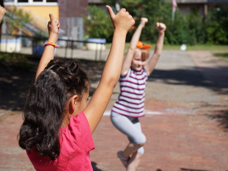 Drei Mädchen heben ihre Arme hoch und zeigen die Daumen