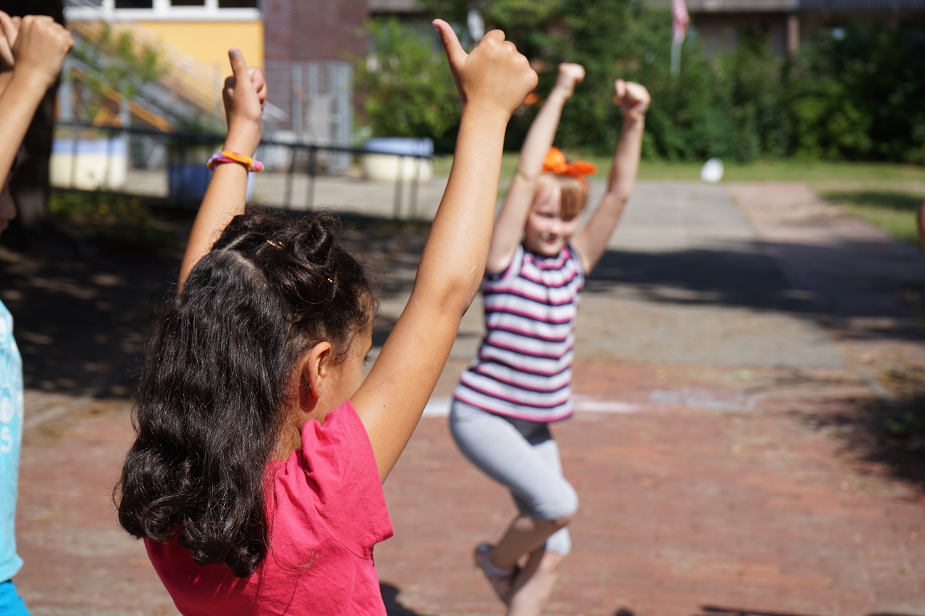 Drei Mädchen heben ihre Arme hoch und zeigen die Daumen