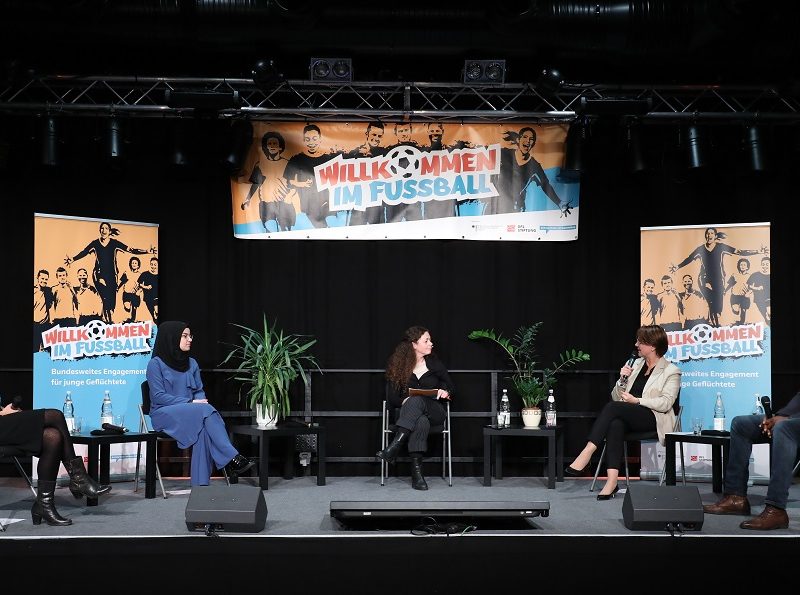 Vier Frauen und ein Mann sitzen auf Stühlen im Halbkreis auf dem Podium