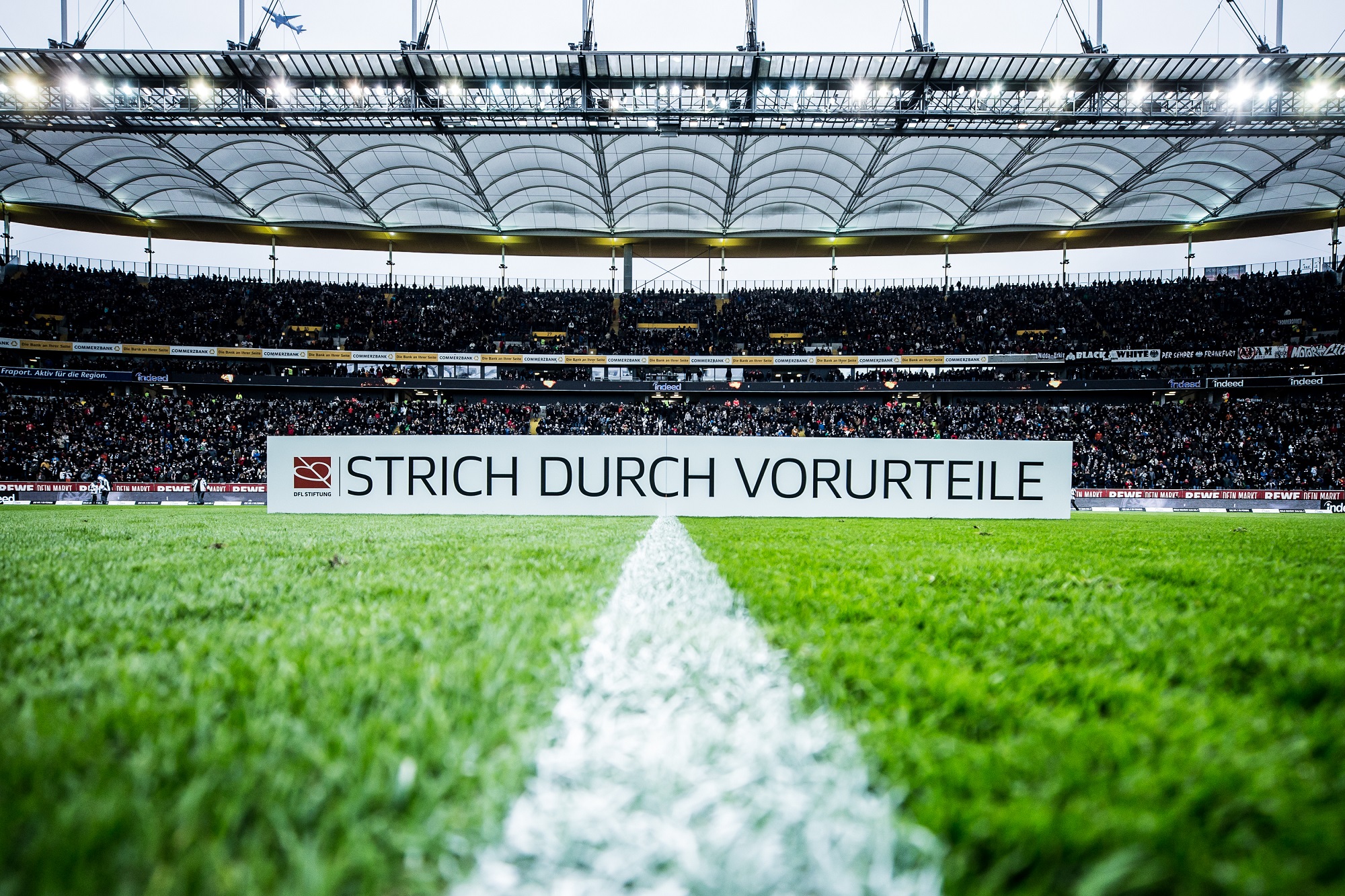 Ein Fußballstadion mit grünem Rasen, auf dem der Schriftzug "STRICH DURCH VORURTEILE" zu sehen ist. Im Hintergrund sind die Tribünen mit Zuschauern gefüllt.
