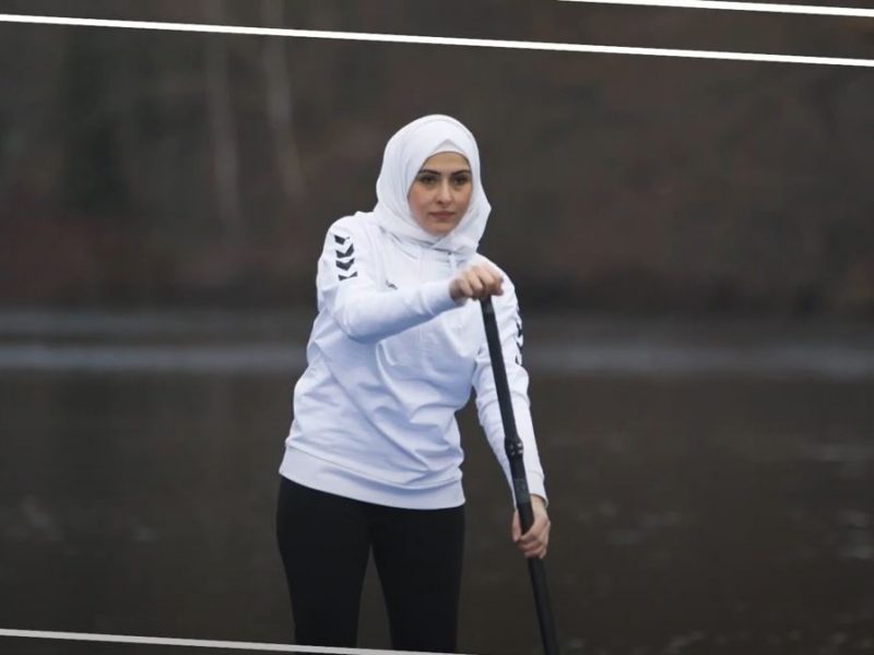 Mädel im weißen Sweatshirt und mit weißem Kopftuch paddelt auf dem See