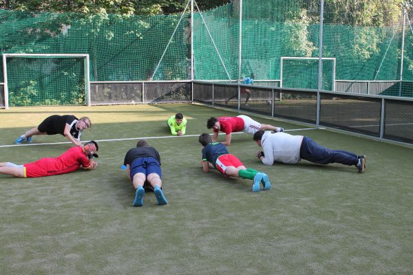 Sieben junge Menschen mit und ohne Behinderung machen gemeinsam auf einem Fußballplatz Kräftigungsübungen.