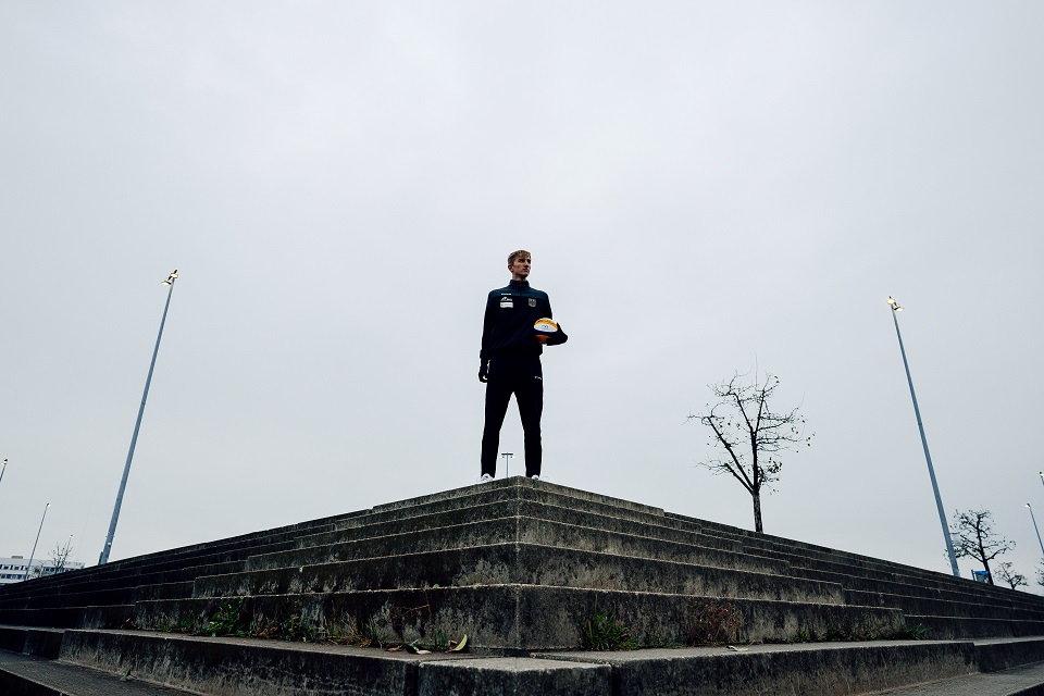 Momme Lorenz steht mit einem Beachvolleyball in der Hand am oberen Ende einer Treppe.