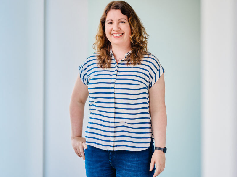 Lena Ziegenhagen, lächelnd, trägt ein blau-weiß gestreiftes Hemd und Jeans.