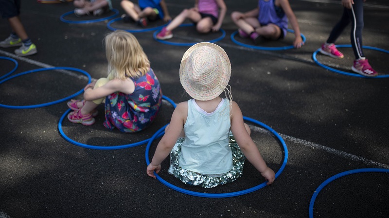Zwei Mädchen sitzen auf dem Boden einer Leichtathletikbahn. Sie sitzen in blauen Sportreifen.